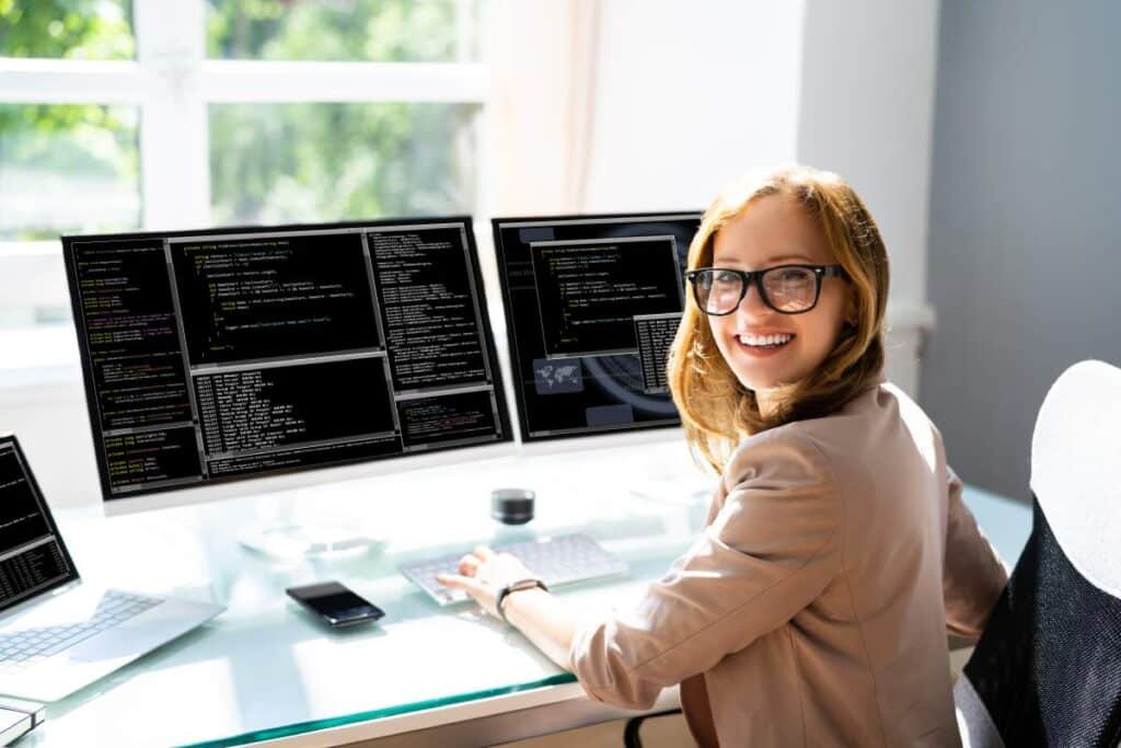 A smiling programmer works on source code on dual monitors